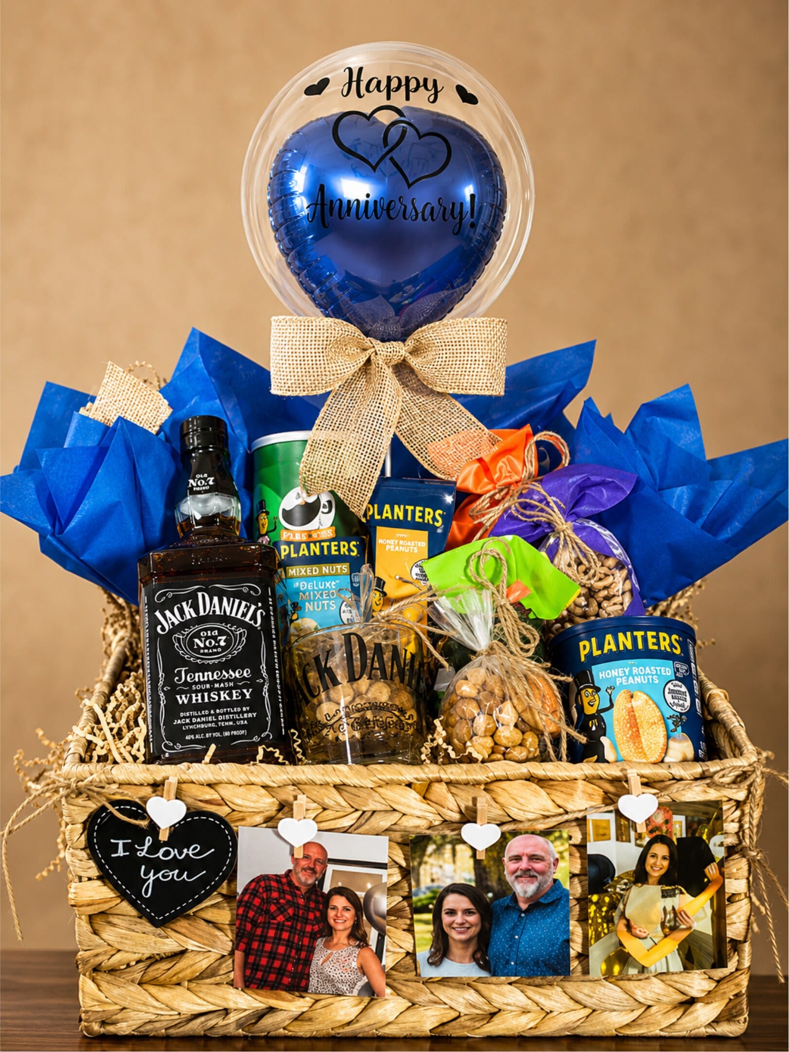 A blue personalised balloon above a rustic basket with whiskey, snacks, and framed photographs.